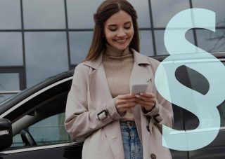 Nainen katsoo kännykkää lasiseinäisen rakennuksen edessä